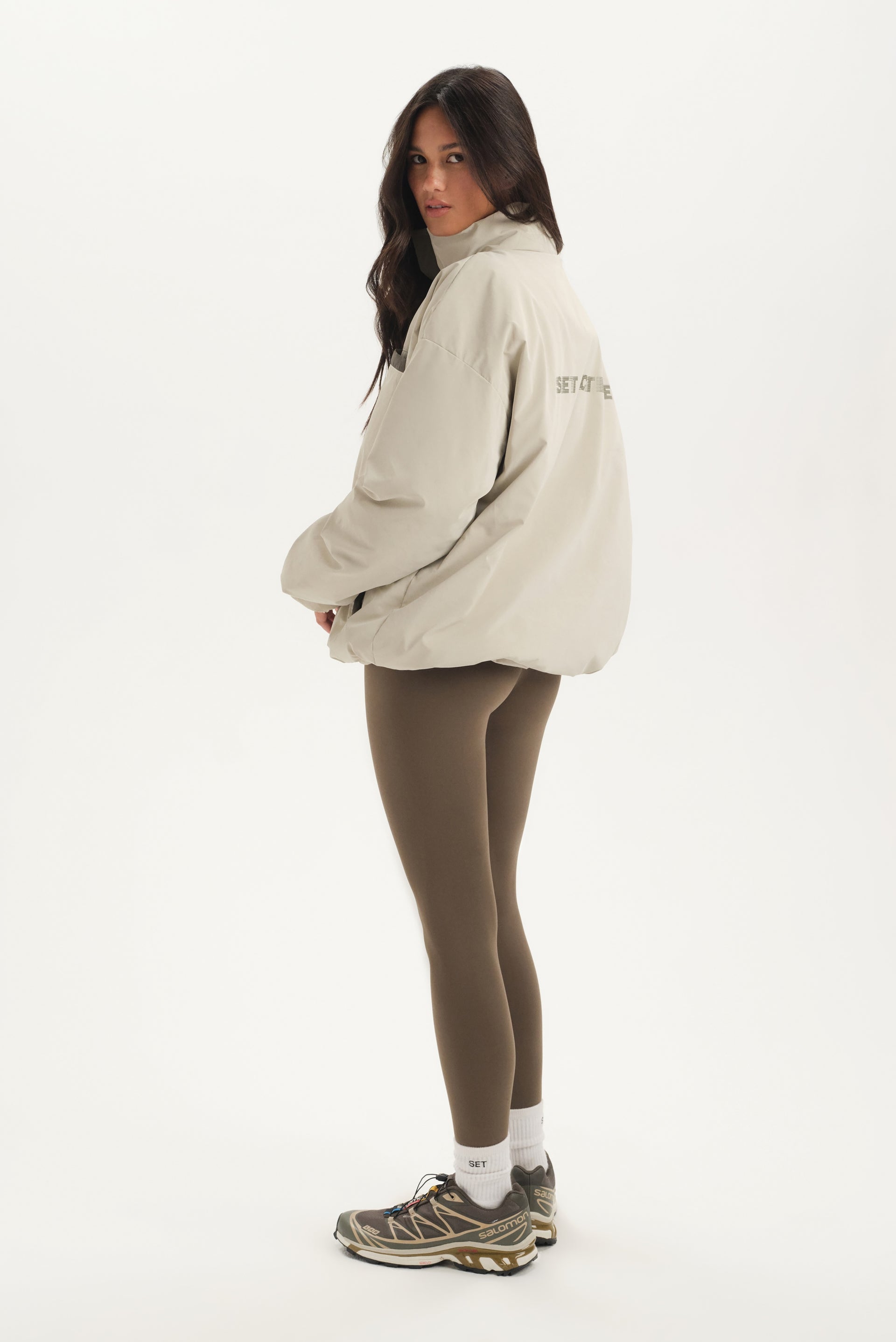 Woman wearing a beige jacket and brown leggings on a white background