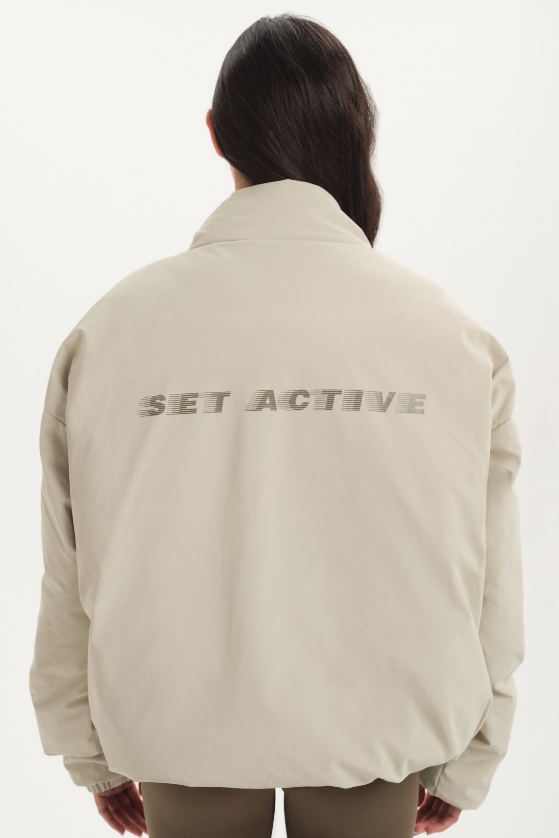 Person wearing a beige jacket with 'SET ACTIVE' text on the back against a white background
