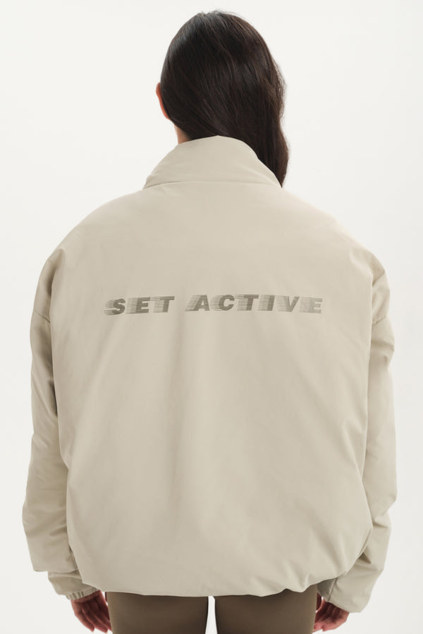 Person wearing a beige jacket with 'SET ACTIVE' text on the back against a white background