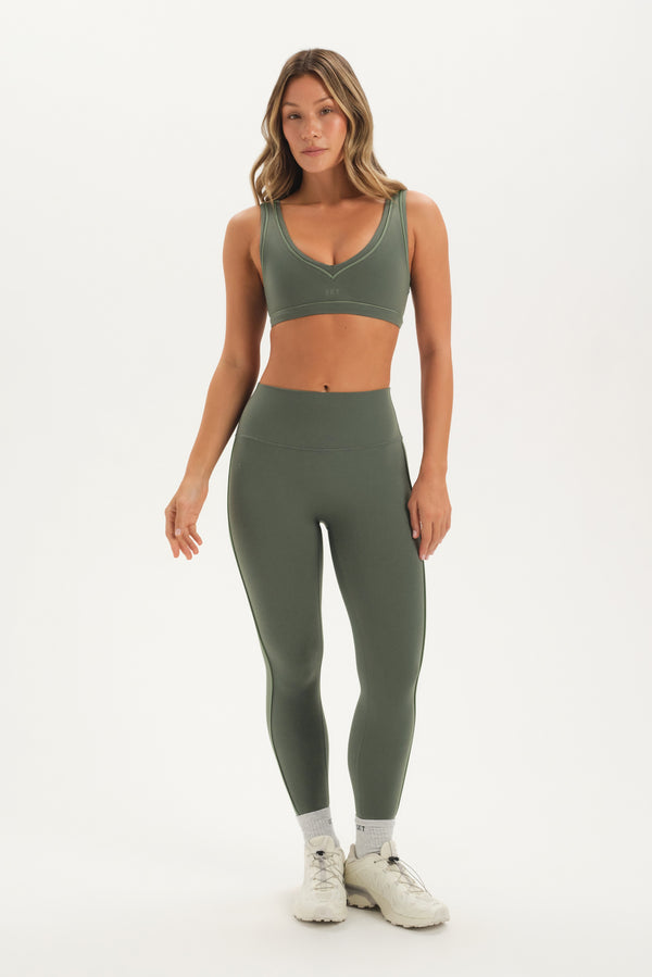 Woman wearing a green sports bra and leggings set on a white background