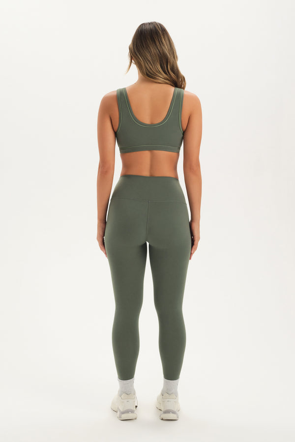 Woman wearing a green sports bra and leggings set on a white background
