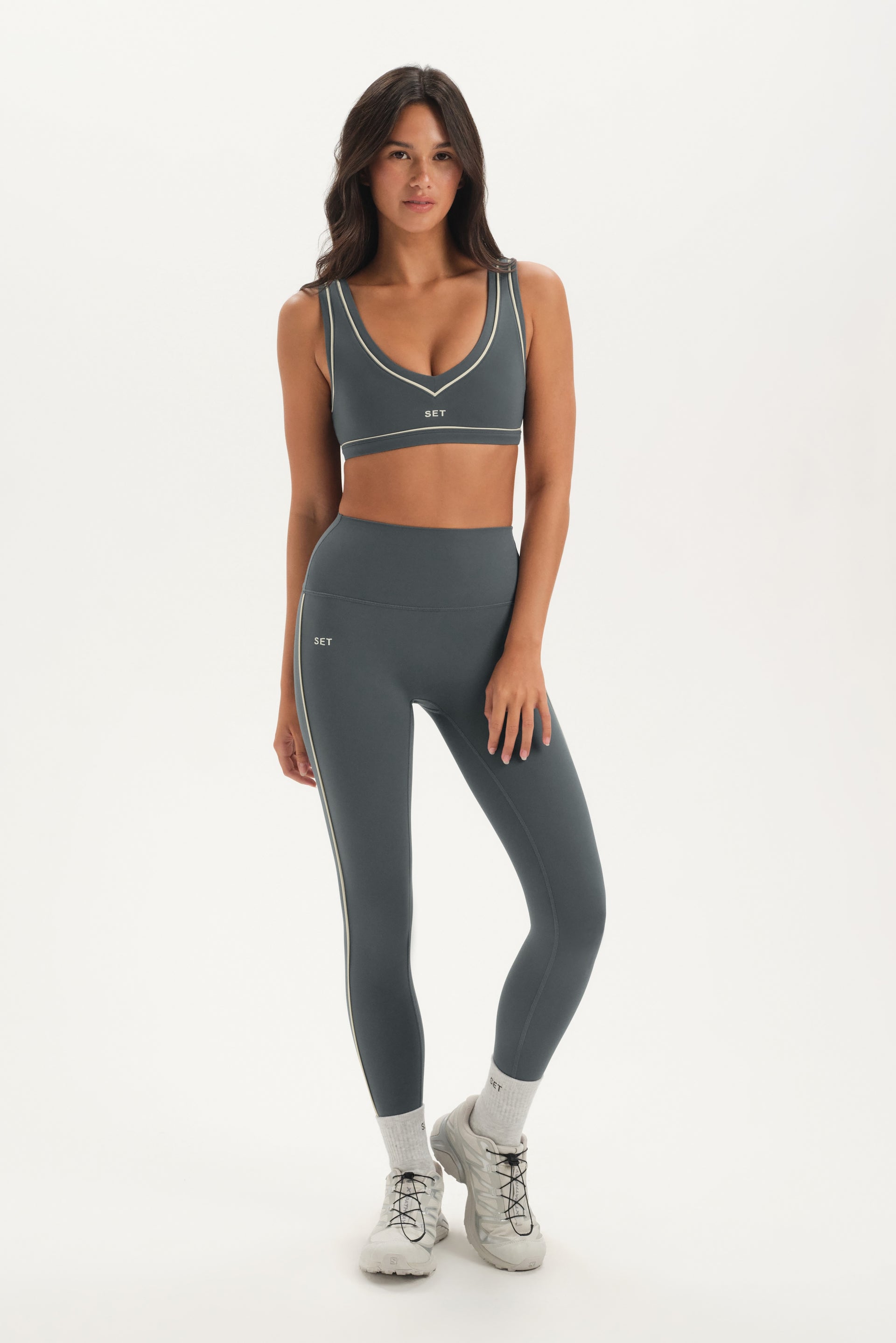 Woman wearing a gray sports bra and leggings set on a white background 