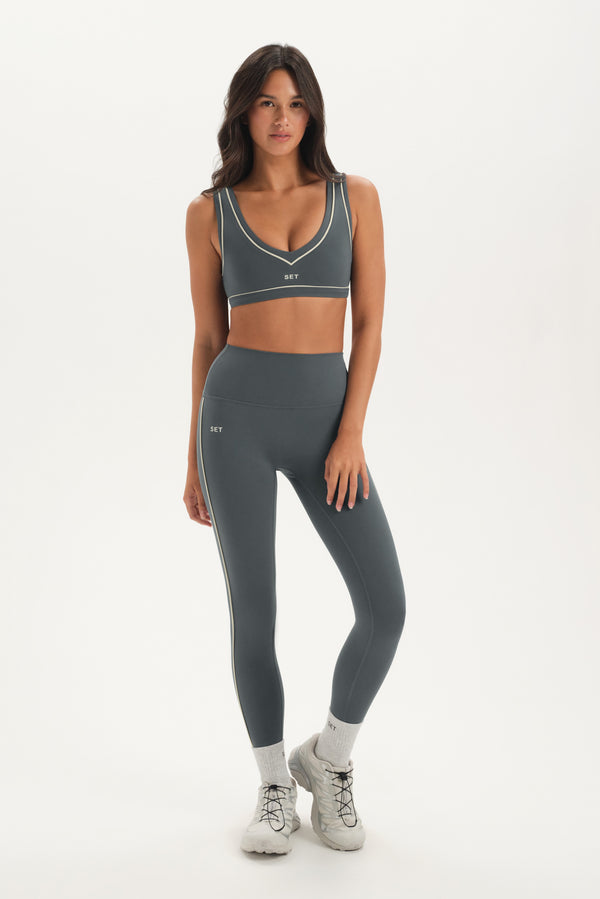 Woman wearing a gray sports bra and leggings set on a white background