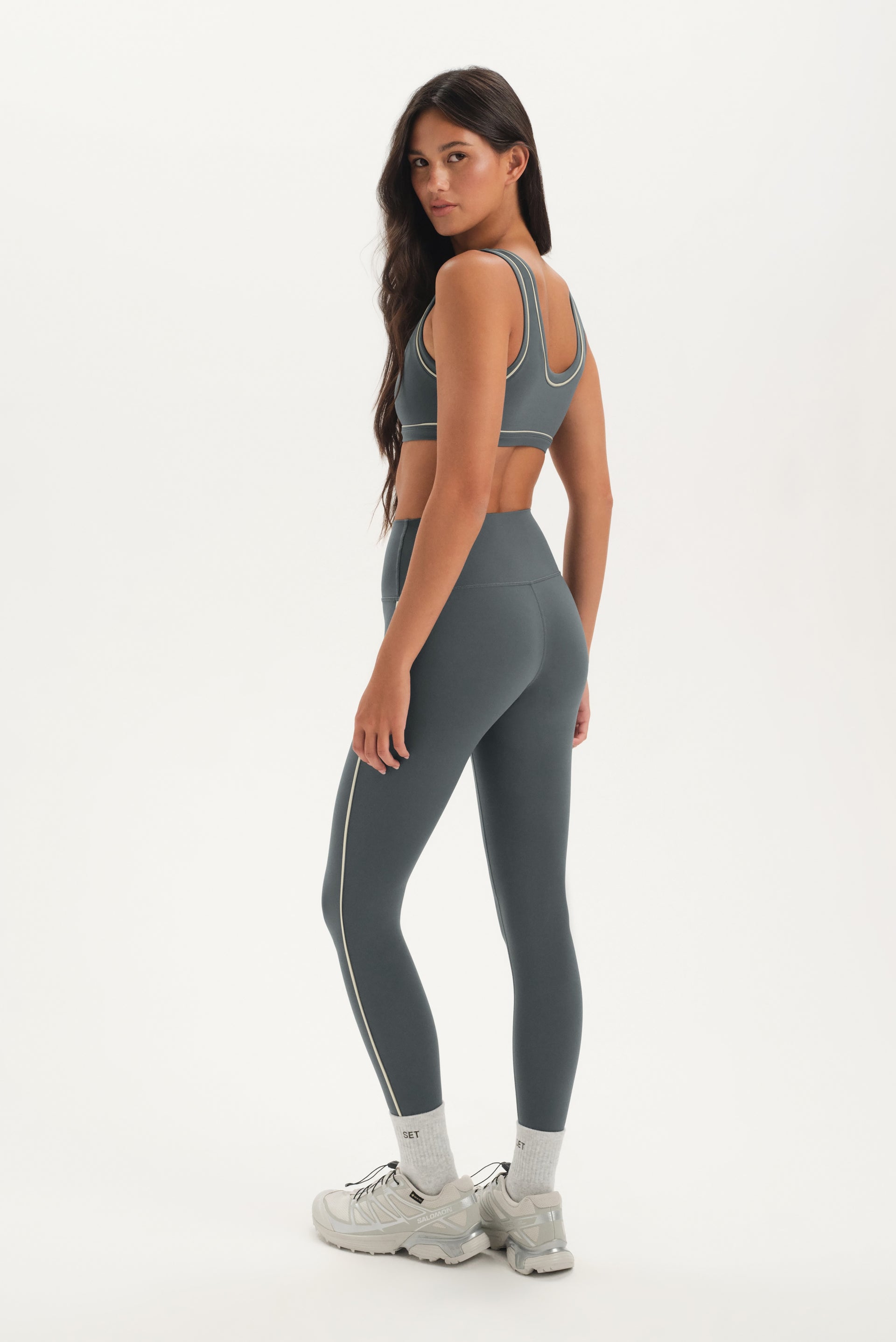 Woman wearing a gray sports bra and leggings set on a white background