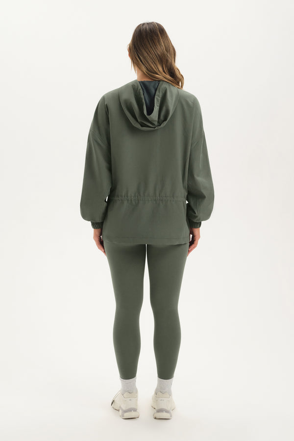 Person wearing a green hoodie and leggings set on a white background