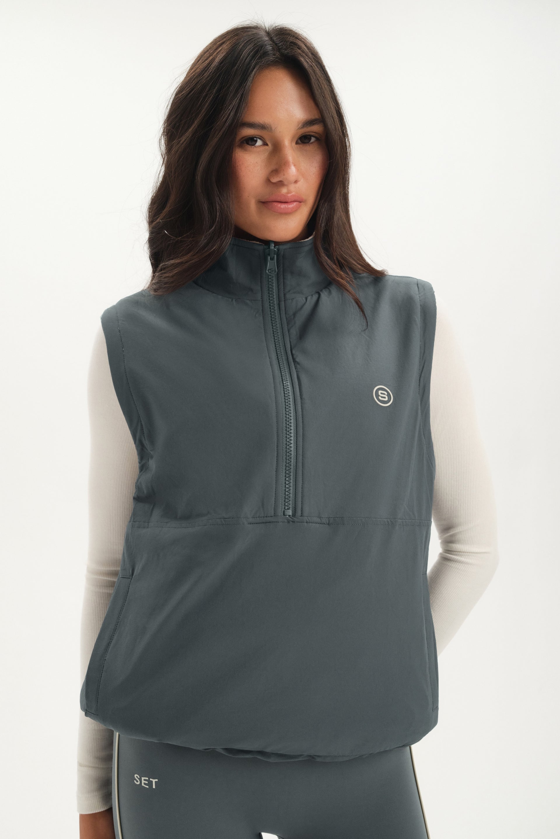 Woman wearing a gray vest with a brand logo on a white background <model-info>Jelene wears a size XS and is 5’7”, 23” waist, 32AB bust.</model-info>