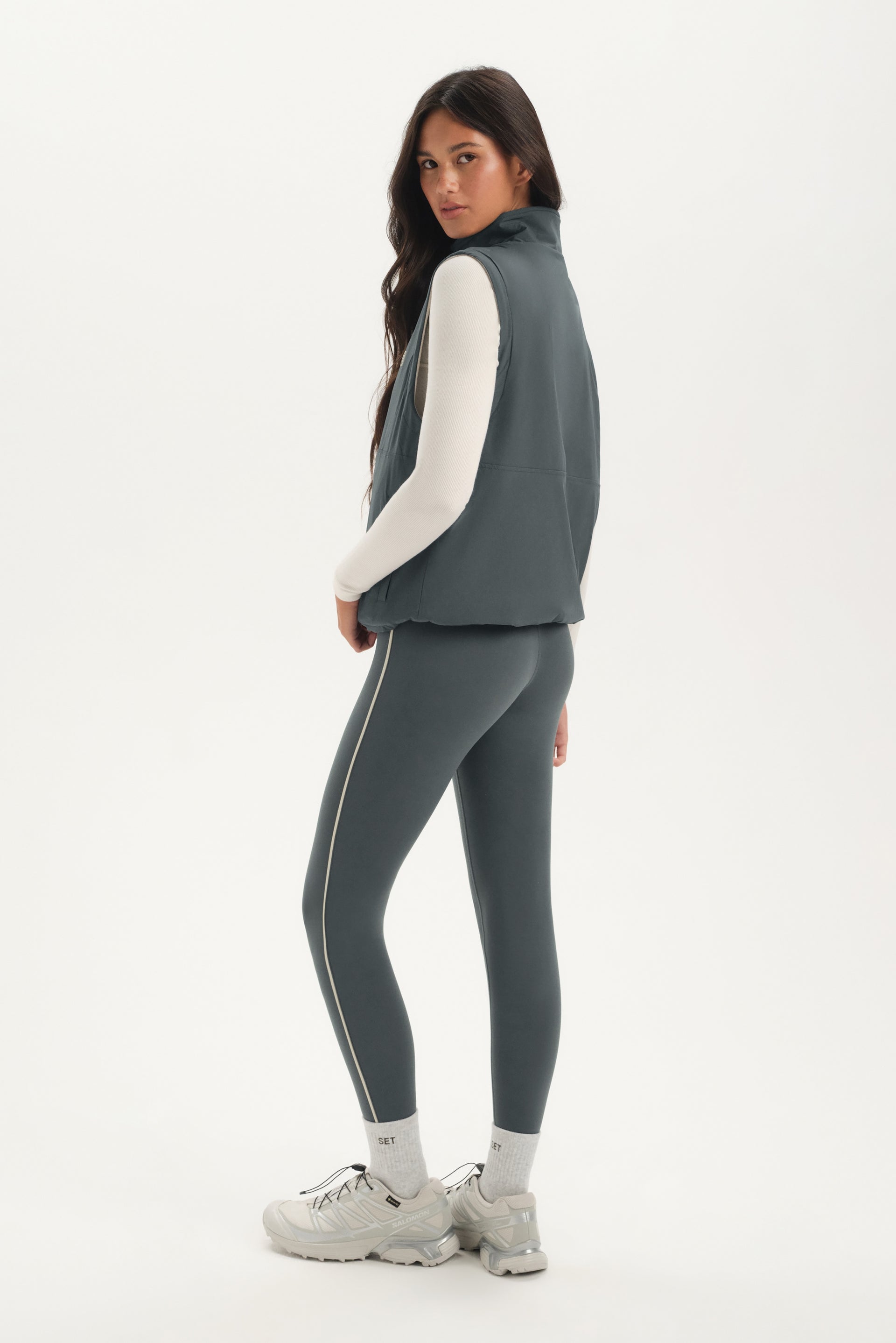 Woman wearing a gray vest and leggings with white accents on a white background