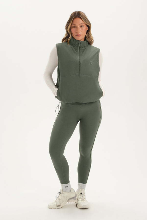 Woman wearing a green vest and leggings set on a white background