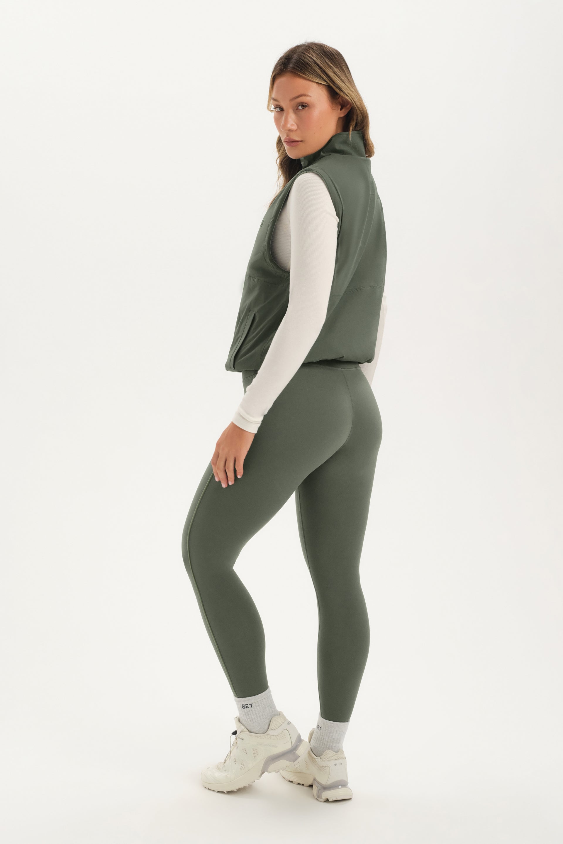 Woman wearing a green vest and leggings on a white background