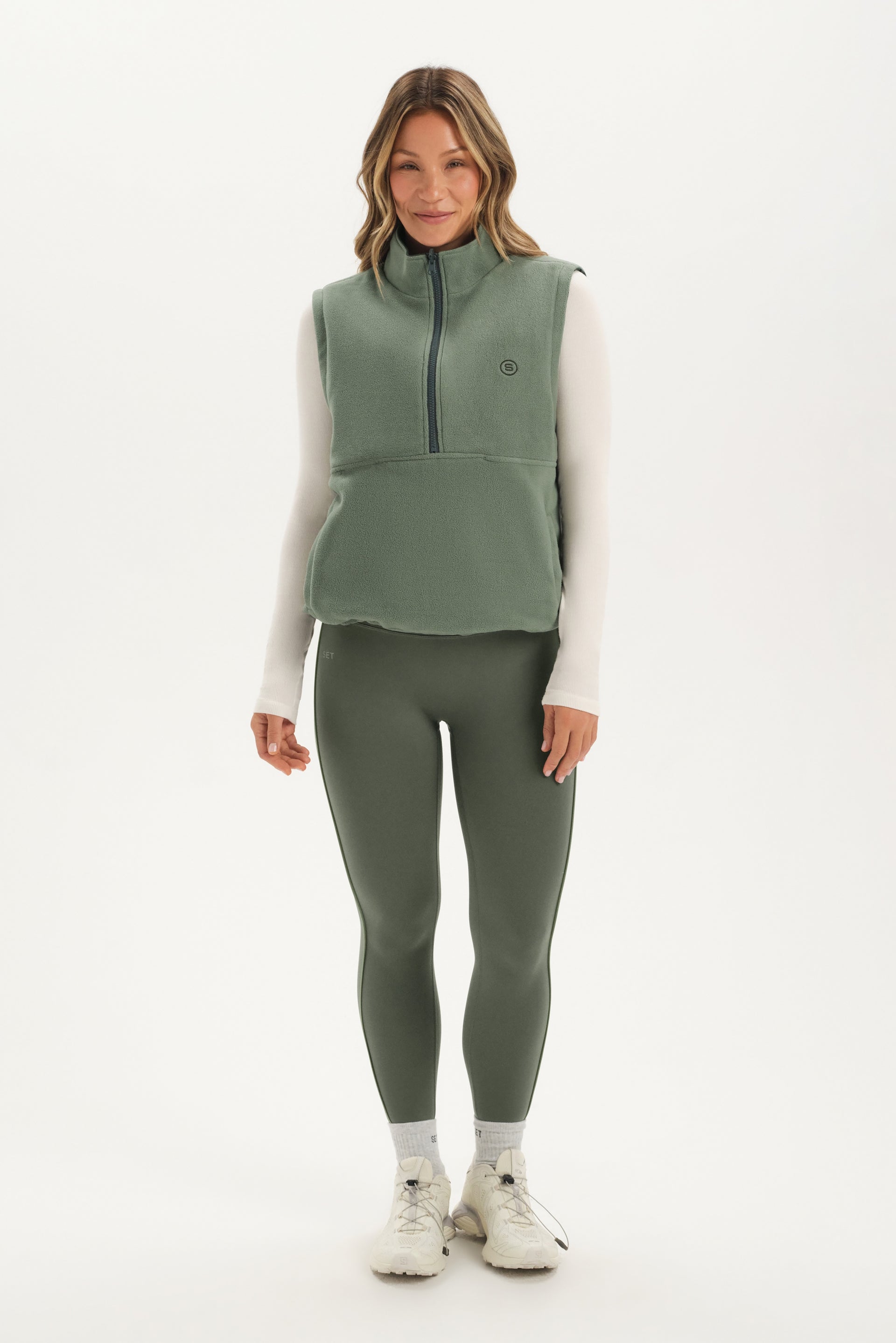 Woman wearing a green vest and leggings set on a white background