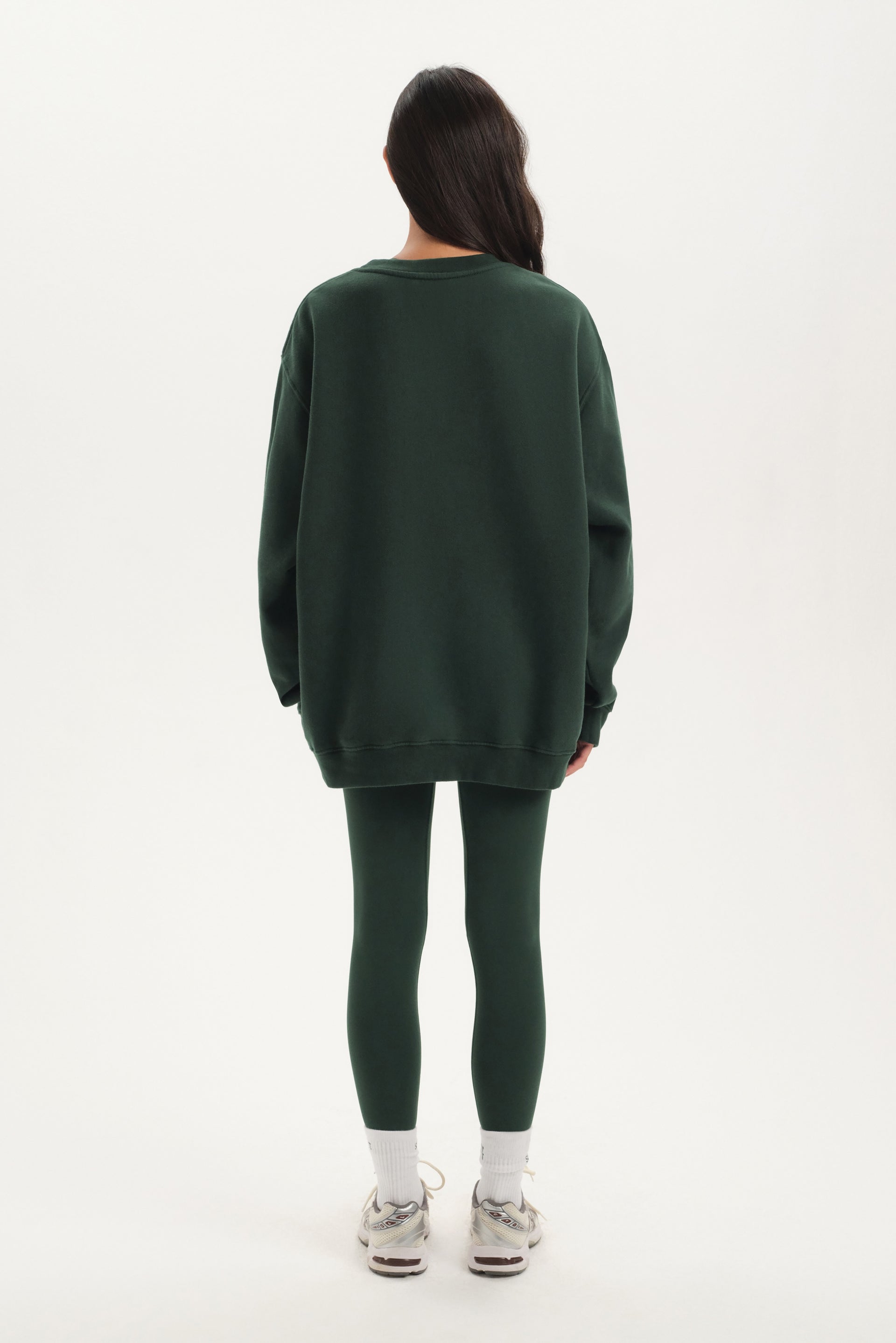 Person wearing a green oversized sweater and leggings set on a white background