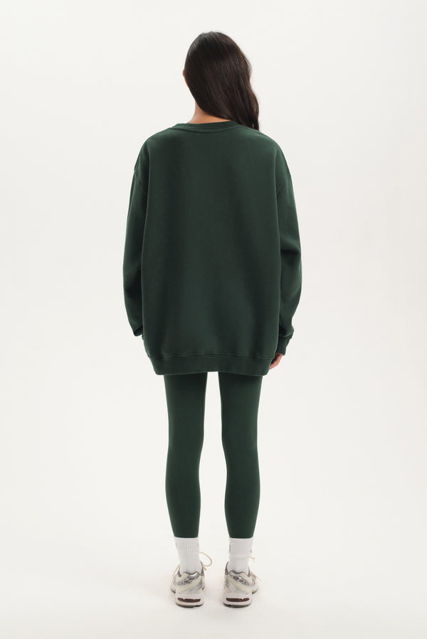Person wearing a green oversized sweater and leggings set on a white background