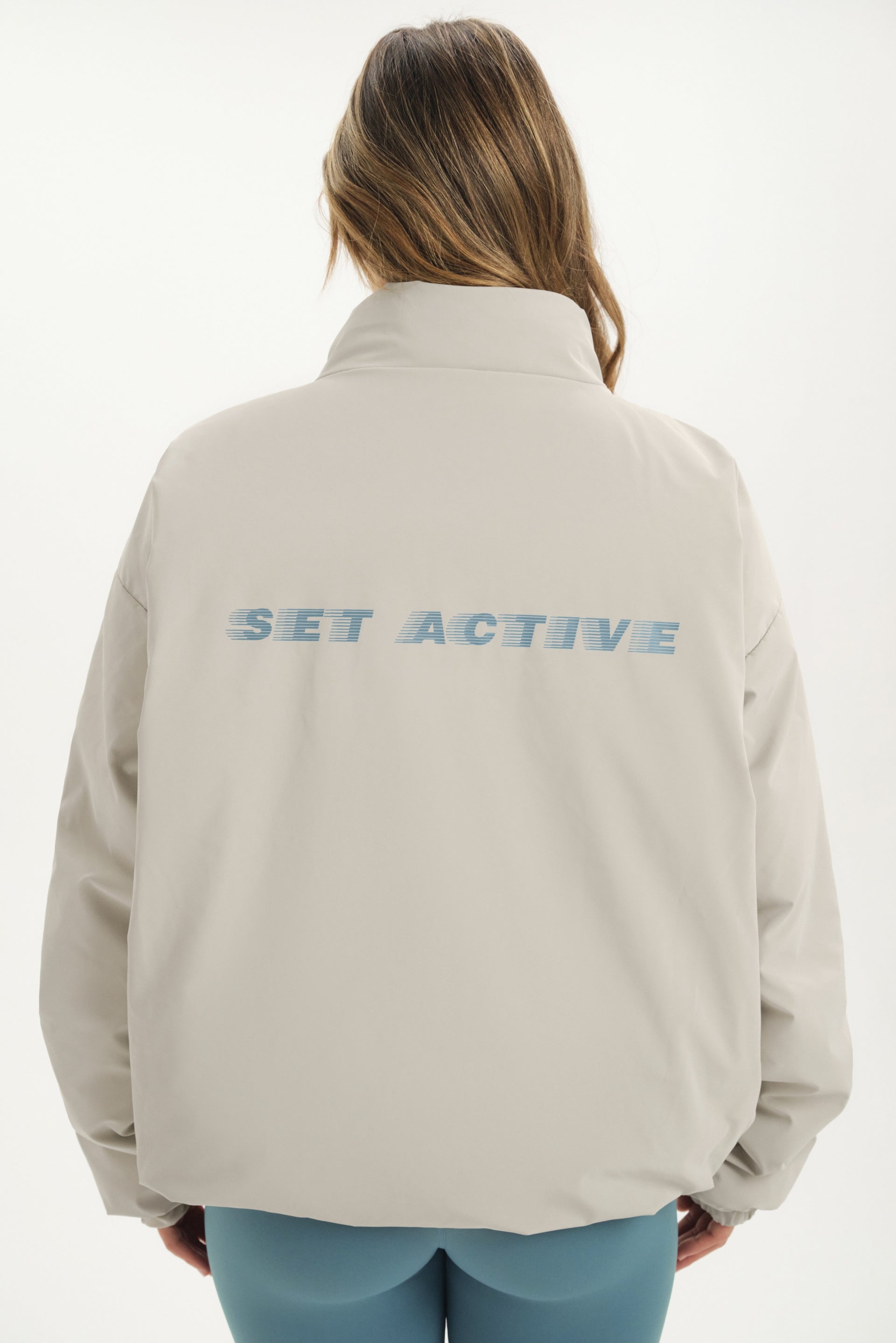 Person wearing a beige jacket with 'SET ACTIVE' text on the back against a white background