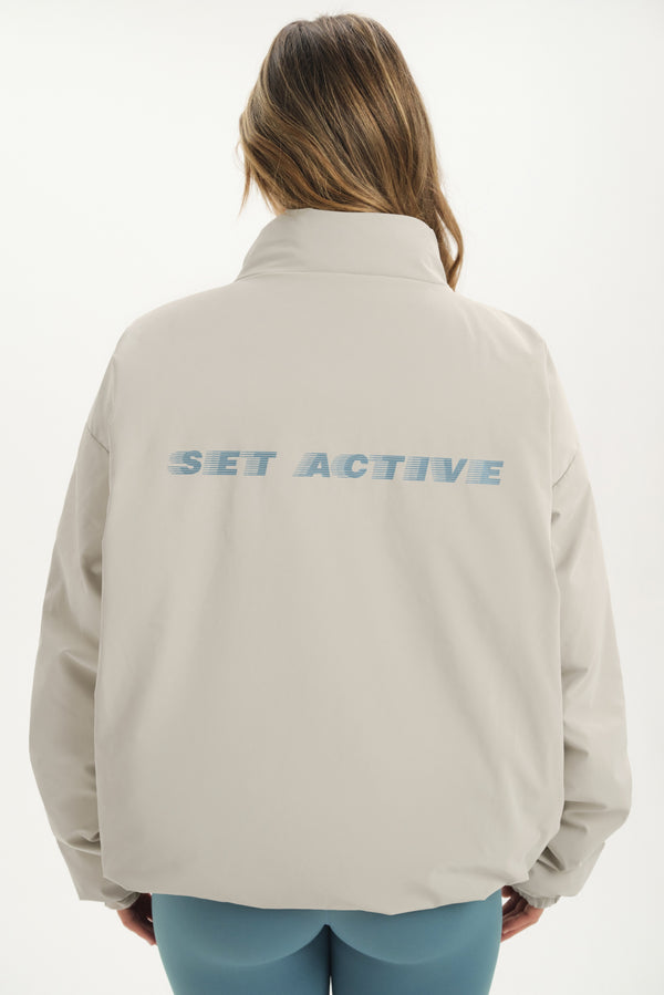 Person wearing a beige jacket with 'SET ACTIVE' text on the back against a white background