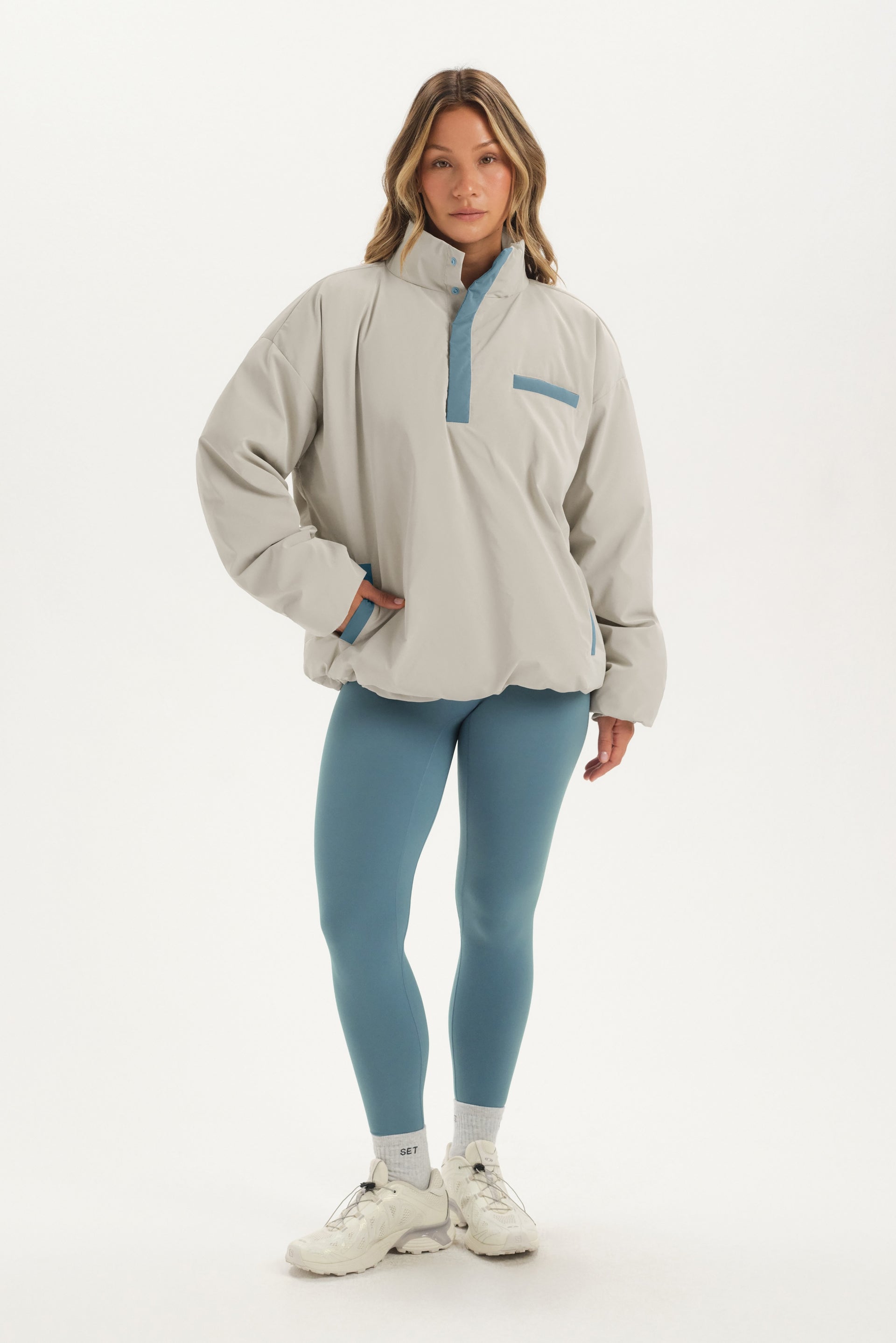 Woman wearing a beige pullover with a blue zipper and matching leggings on a white background