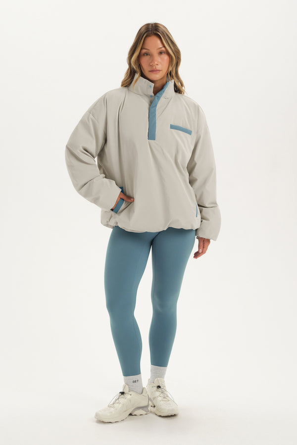Woman wearing a beige pullover with a blue zipper and matching leggings on a white background