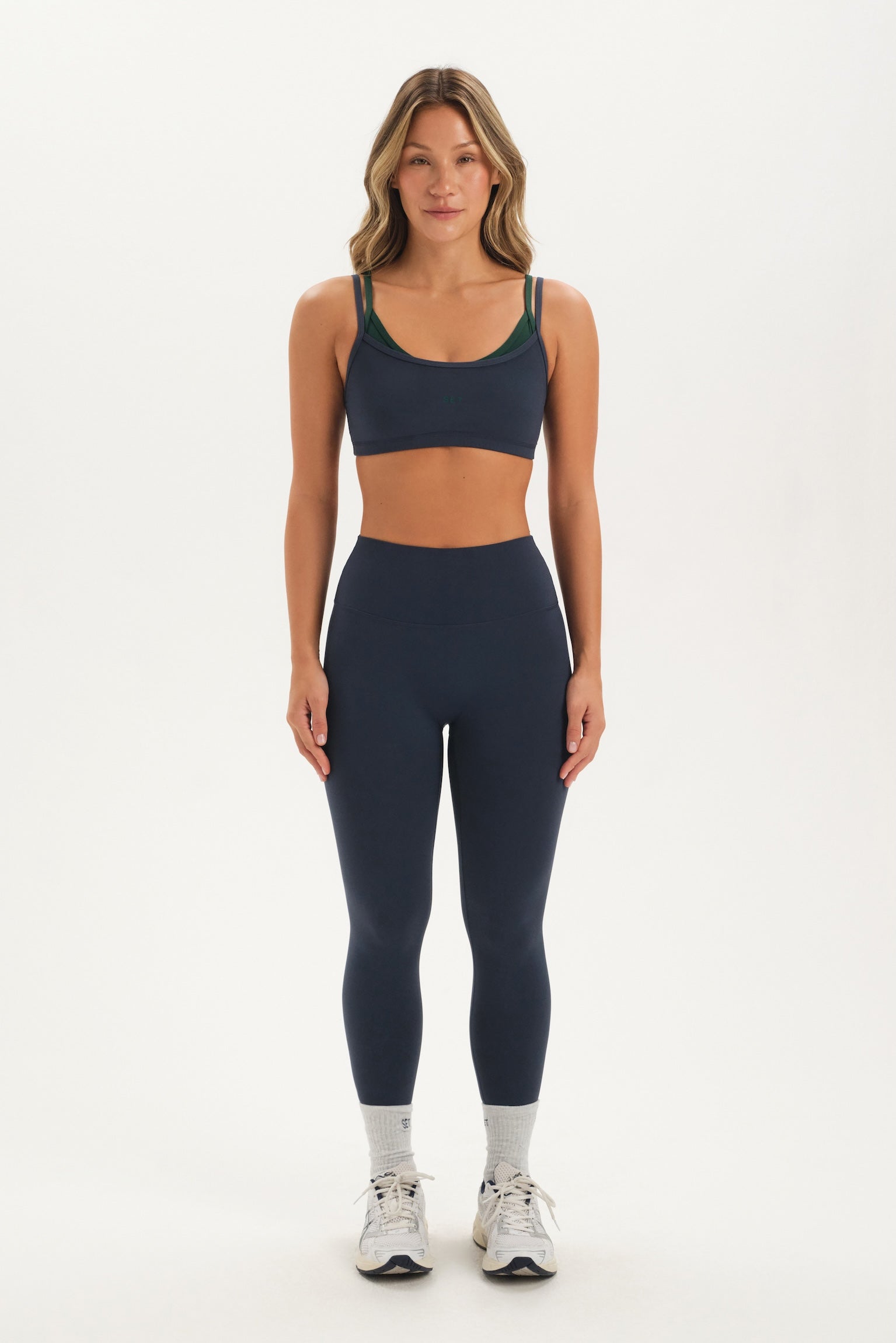 Woman wearing a navy sports bra and leggings set on a white background