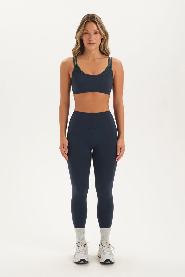 Woman wearing a navy sports bra and leggings set on a white background