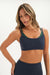 Woman wearing a dark blue sports bra with green straps on a white background <model-info>Bre wears a size S and is 5’7”, 25½" waist, 33” bust.</model-info>