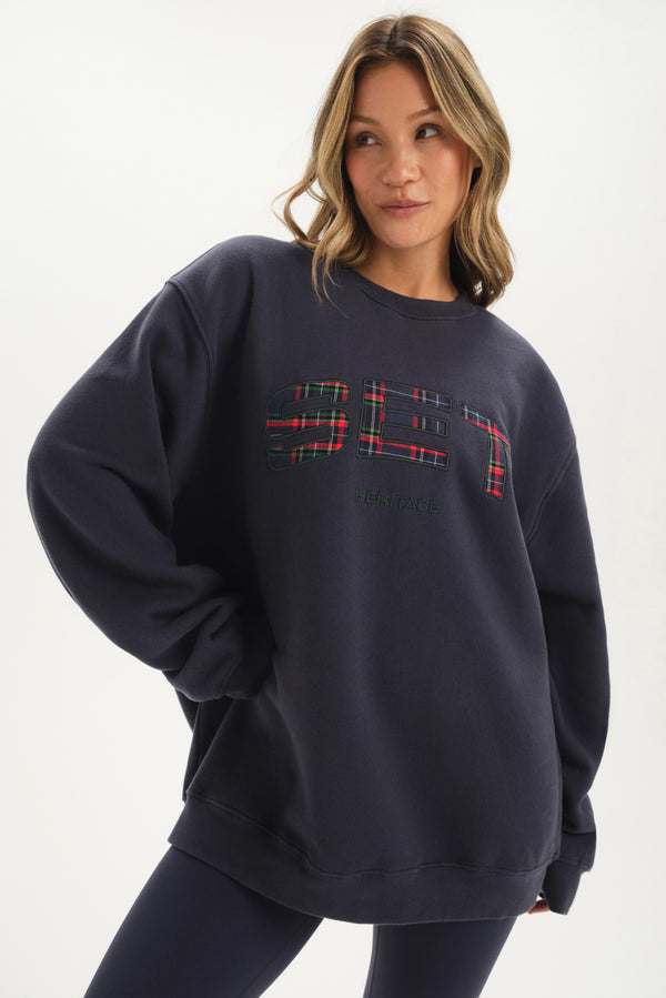 Person wearing a navy sweatshirt with a plaid design on a white background 