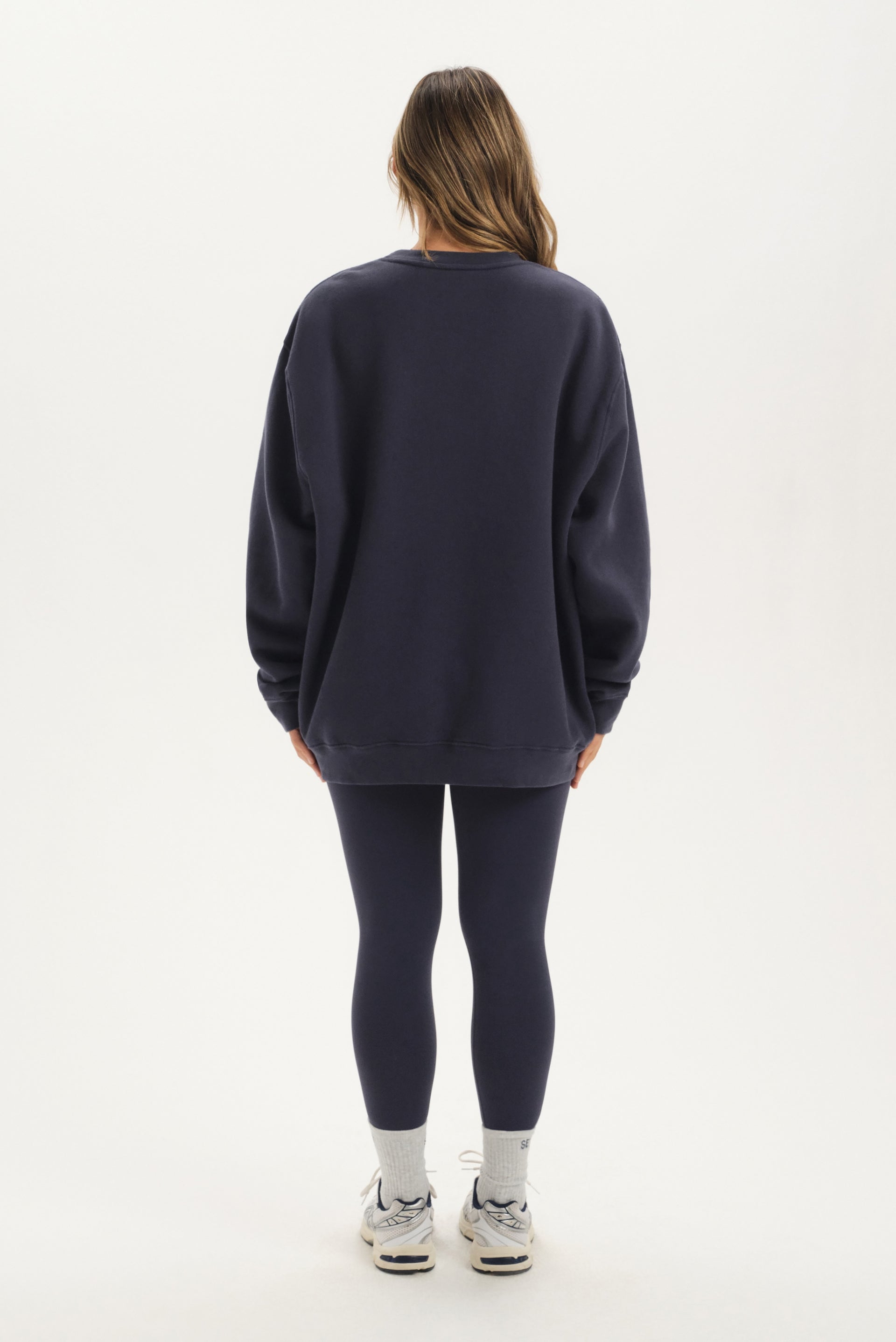 Person wearing a navy oversized sweatshirt and leggings on a white background