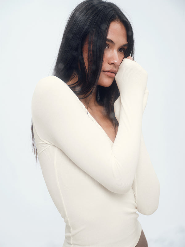 Woman wearing a white long-sleeve top against a plain background
