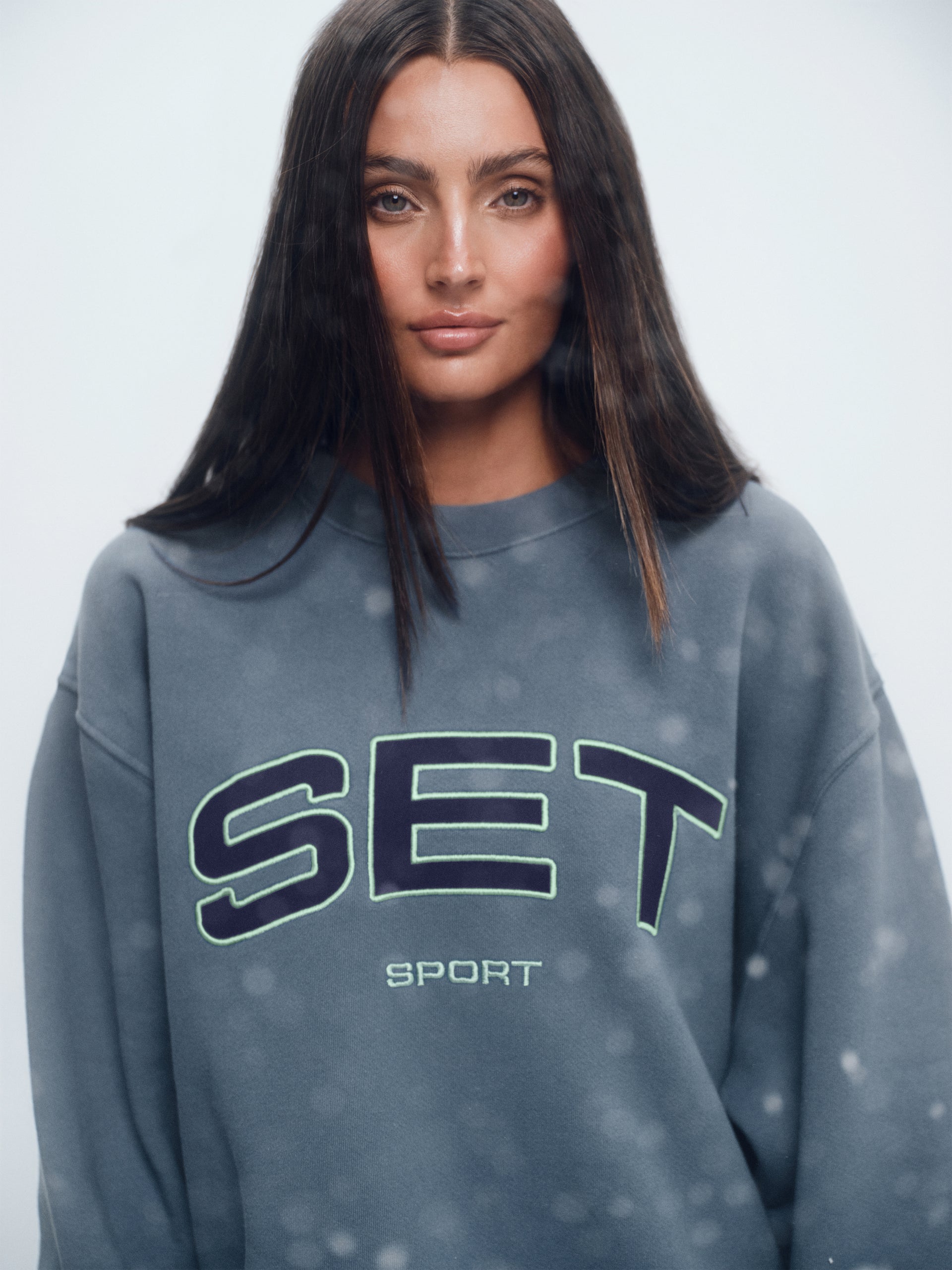 Woman wearing a gray sweatshirt with 'SET Sport' branding on a light gray background