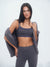 Woman wearing a gray sports bra and leggings with a gray jacket over her shoulder on a white background