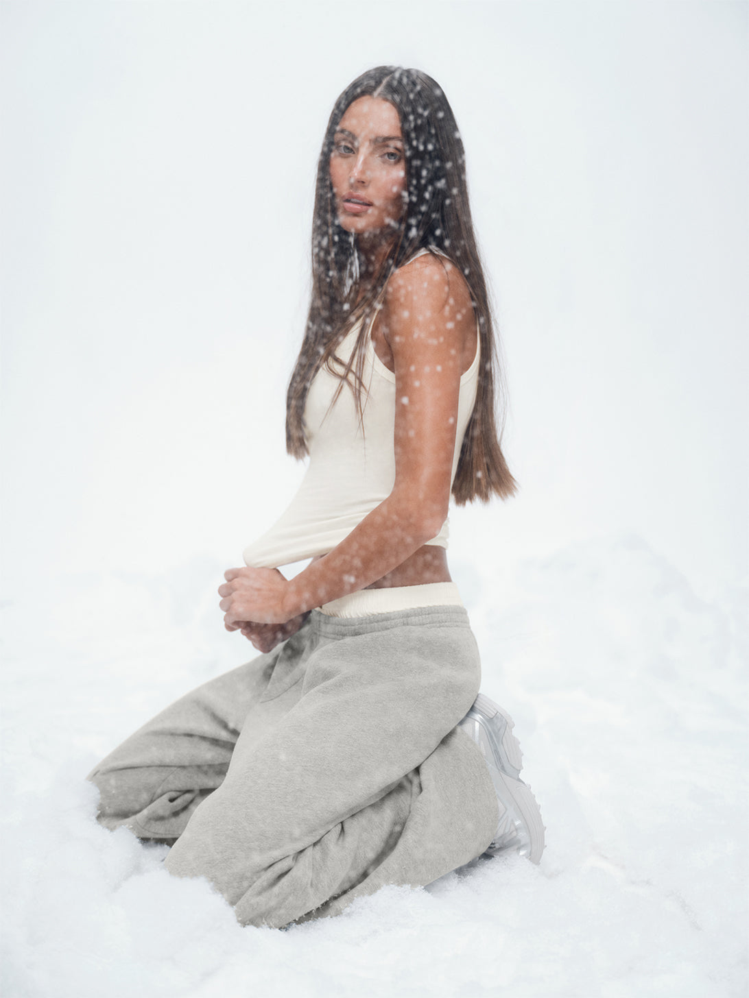 Person wearing a white top and gray pants sitting on a snowy surface.