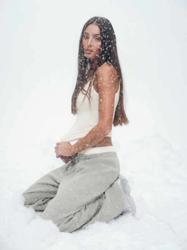 Person wearing a white top and gray pants sitting on a snowy surface.
