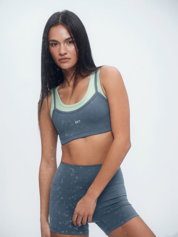 Woman wearing a gray sports bra and shorts with a white background