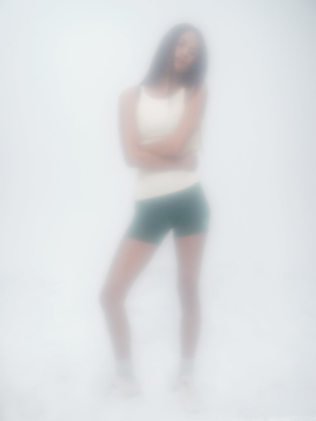 Blurred image of a person wearing a tank top and shorts on a light gray background