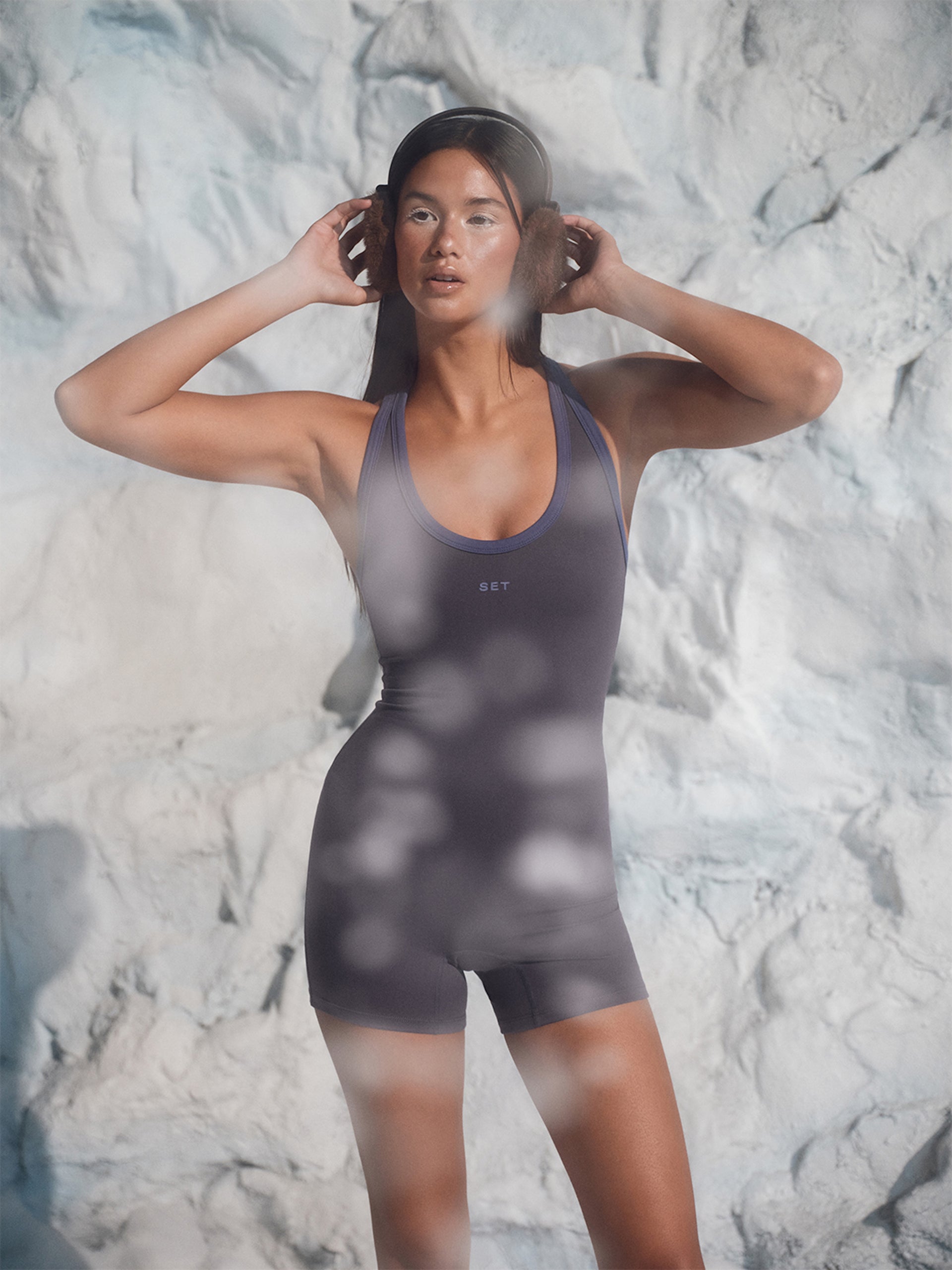Person wearing a dark gray swimsuit against a textured white background