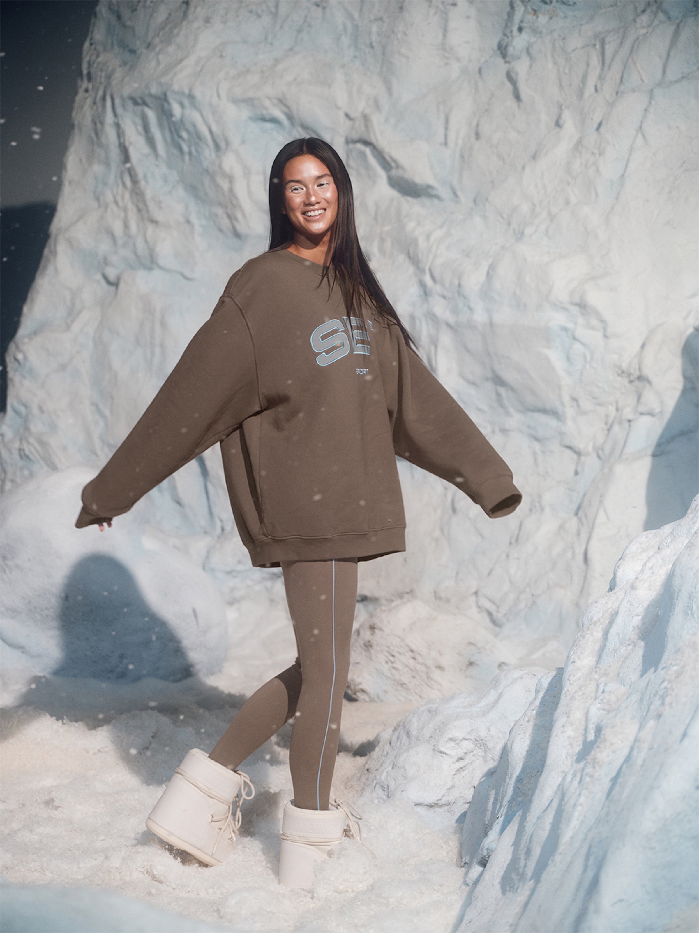 Person wearing a brown sweatshirt and leggings standing in front of a snowy landscape