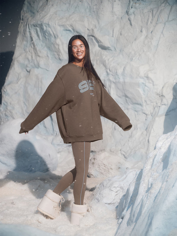 Person wearing a brown sweatshirt and leggings standing in front of a snowy landscape
