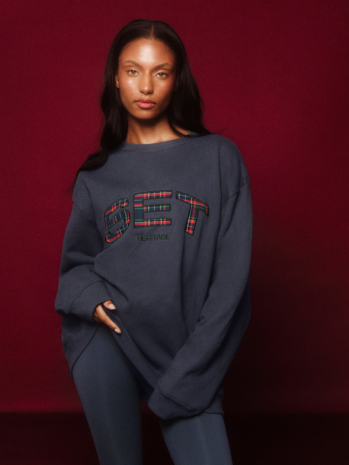 Person wearing a navy sweatshirt with plaid text on a red background <model-info>Sydney wears a size L and is 5’9, 24½” waist, 32B bust.</model-info>