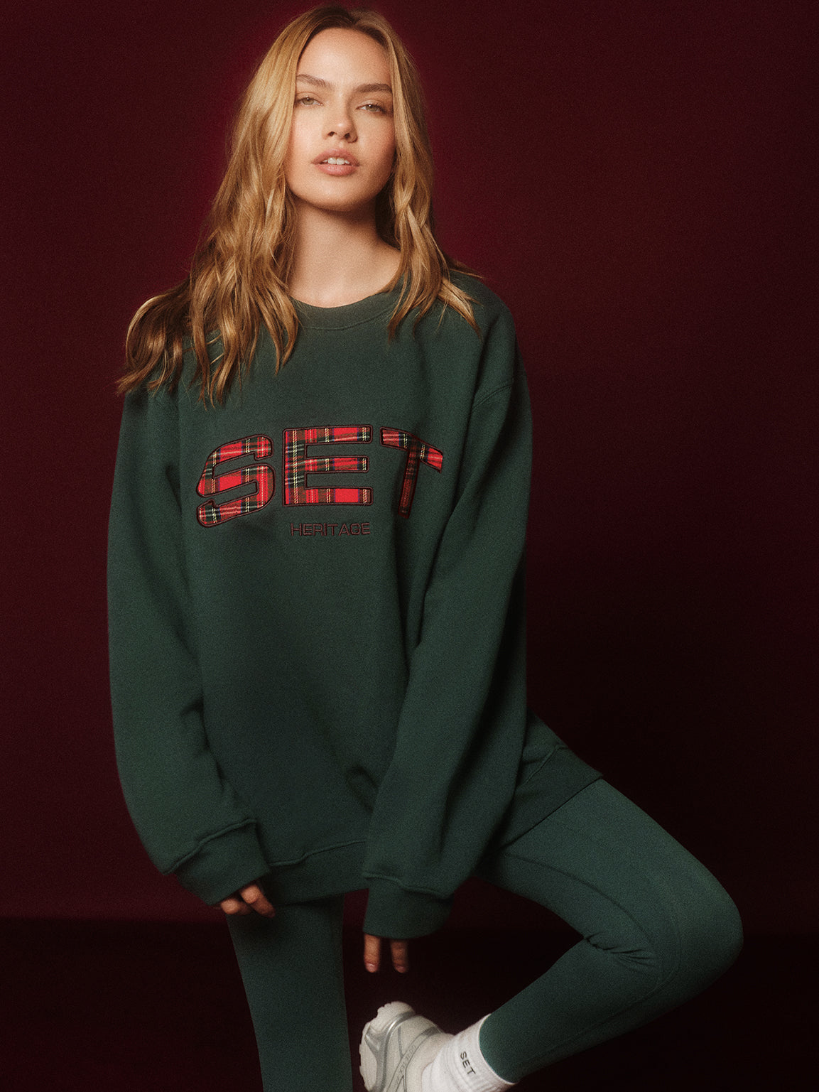 Person wearing a green sweatshirt with a red plaid logo on a dark background