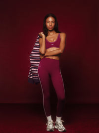 Woman wearing a maroon sports bra and leggings with a striped shirt on a dark red background