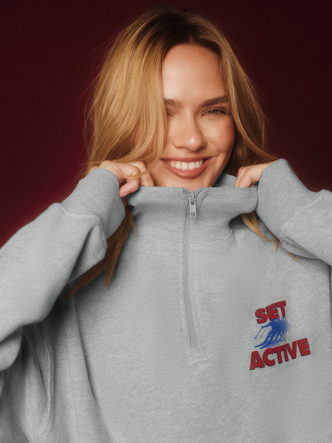Woman wearing a gray hoodie with 'Set Active' logo on a dark red background