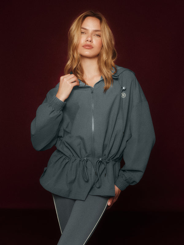 Woman wearing a dark gray cinched windbreaker against a dark background