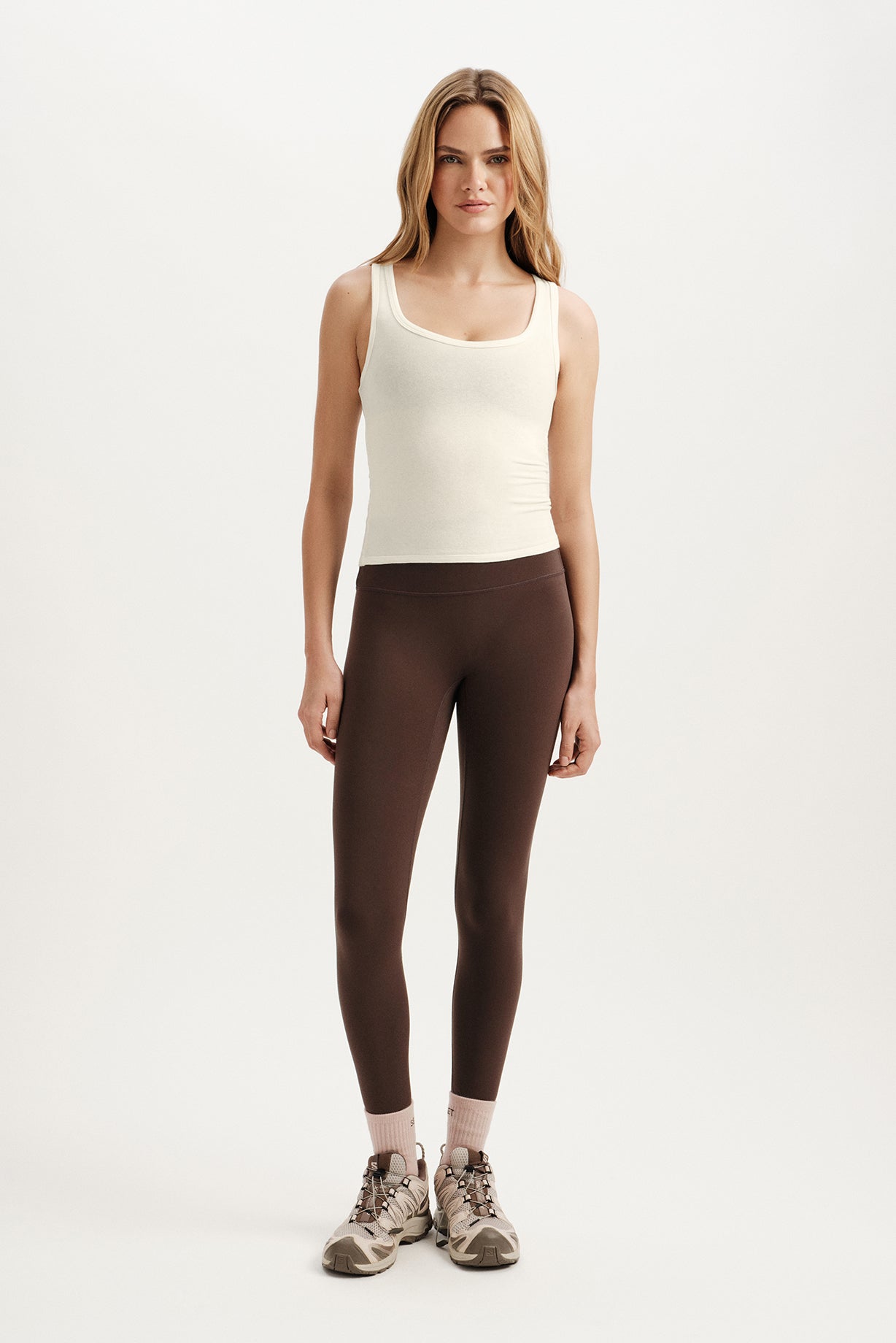 Woman wearing a white tank top and brown leggings on a white background