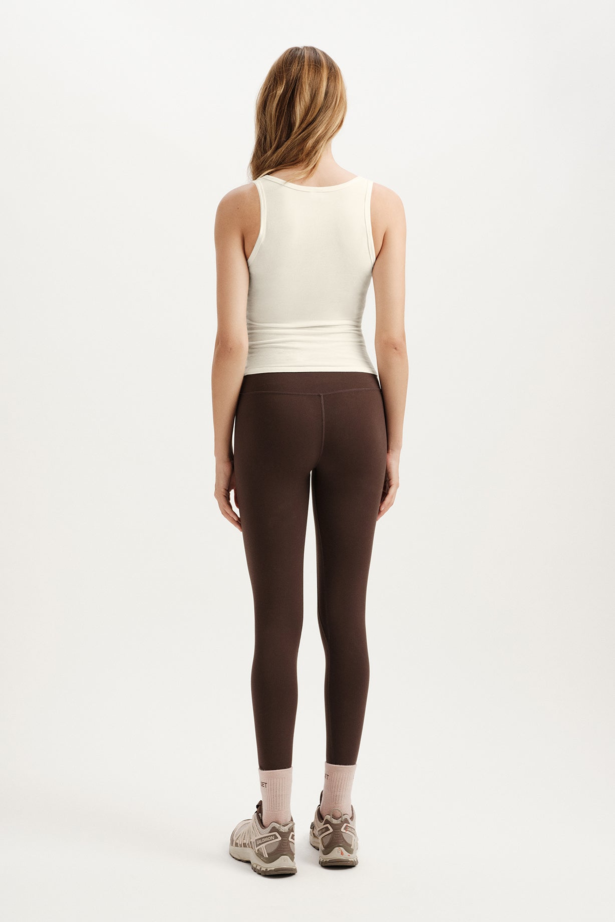 Person wearing a white tank top and brown leggings on a white background