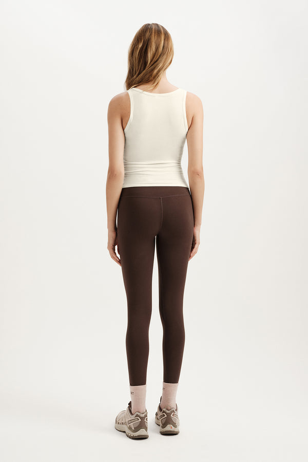 Person wearing a white tank top and brown leggings on a white background
