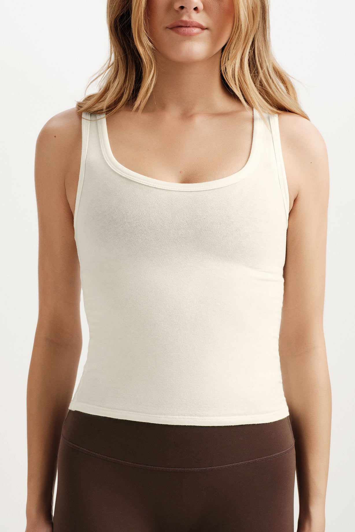 Woman wearing a beige tank top and brown pants on a white background