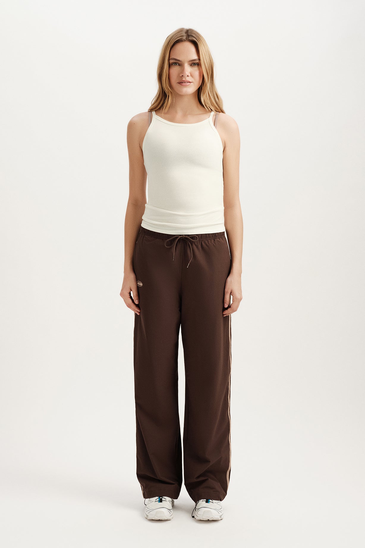 Woman wearing a white sleeveless top and brown pants on a white background