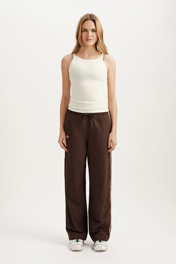 Woman wearing a white sleeveless top and brown pants on a white background