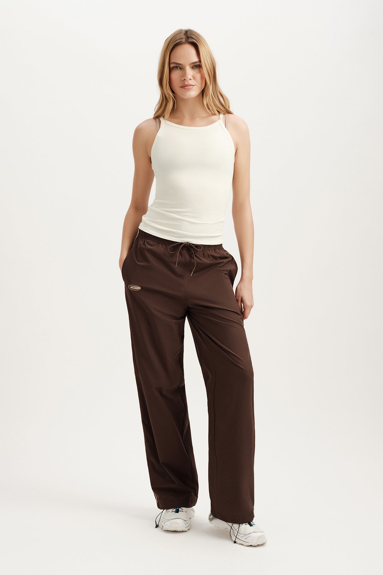 Woman wearing a white tank top and brown pants on a white background