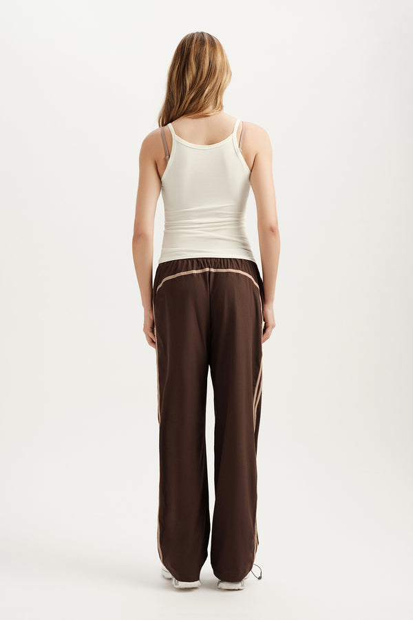 Person wearing a white tank top and brown pants on a white background