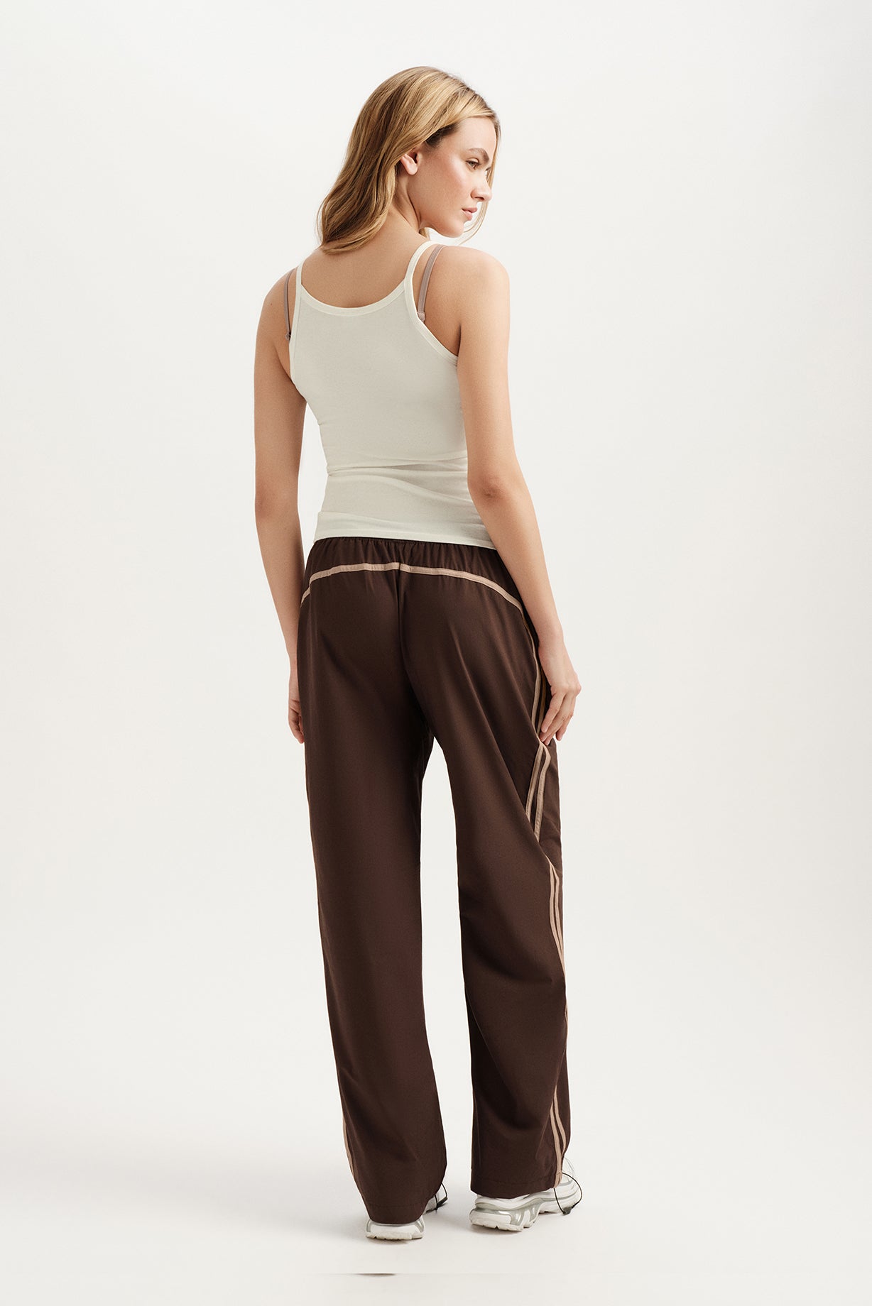 Woman wearing a white tank top and brown pants with a stripe on a white background