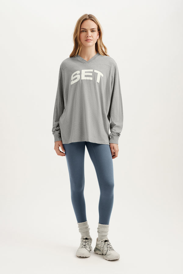 Woman wearing a gray 'SET' sweatshirt, blue leggings, and white sneakers on a white background